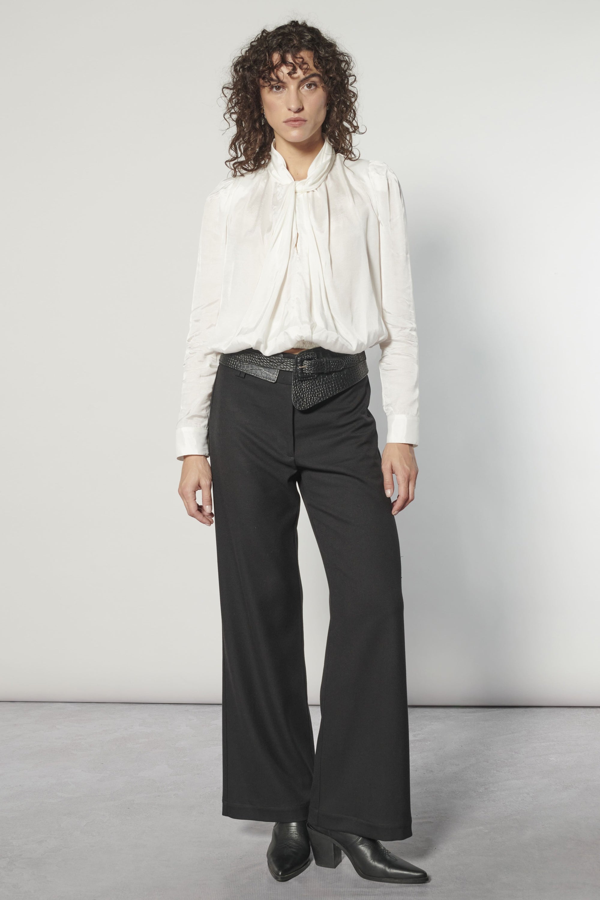 Modelo usando blusa Nord blanca de cuello alto con lazo, calce holgado y pantalón negro