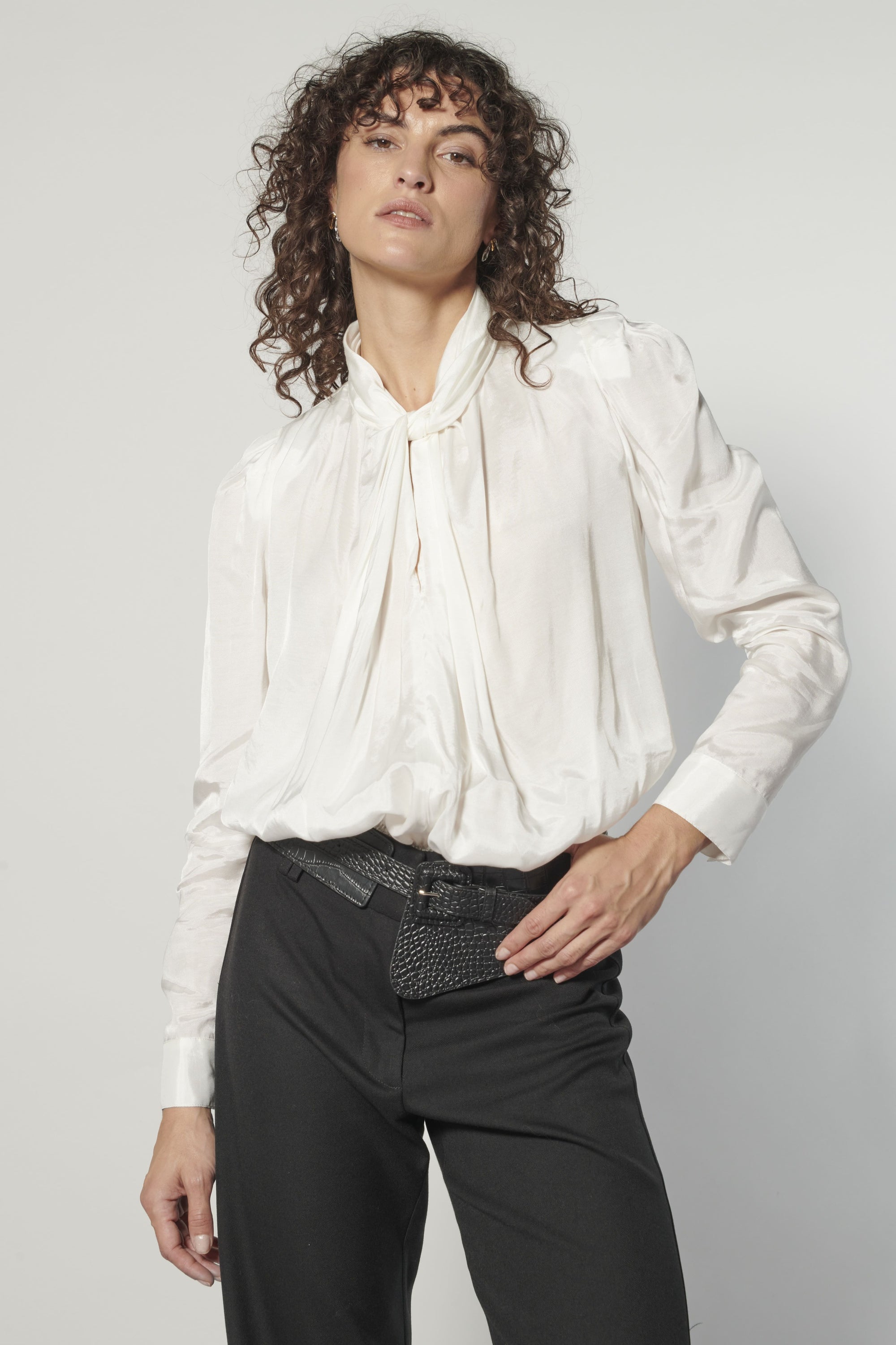 Modelo usando blusa Nord blanca de cuello alto con lazo, calce holgado y pantalón negro