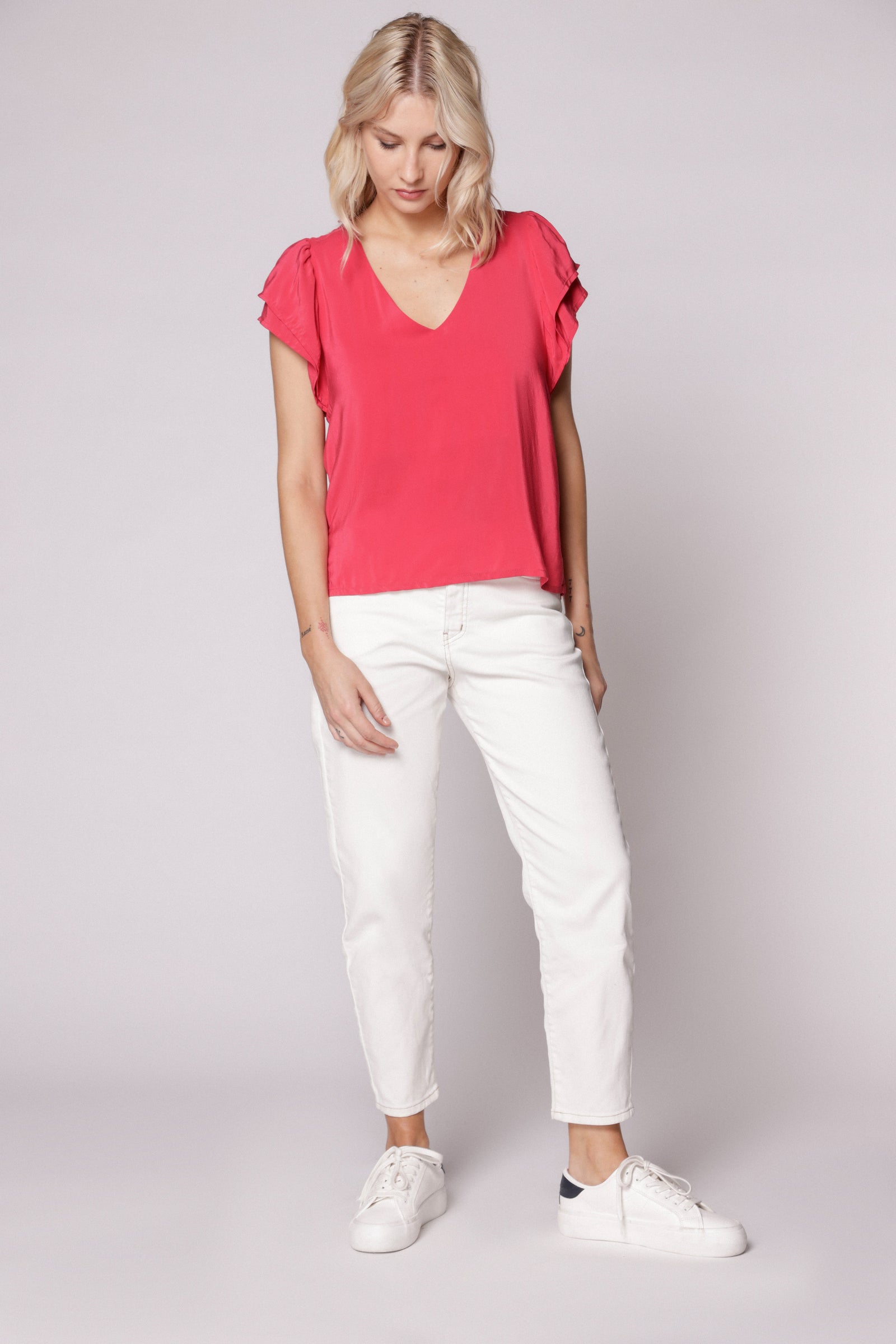 Modelo usando jeans mom fit blanco con blusa fucsia y zapatillas blancas