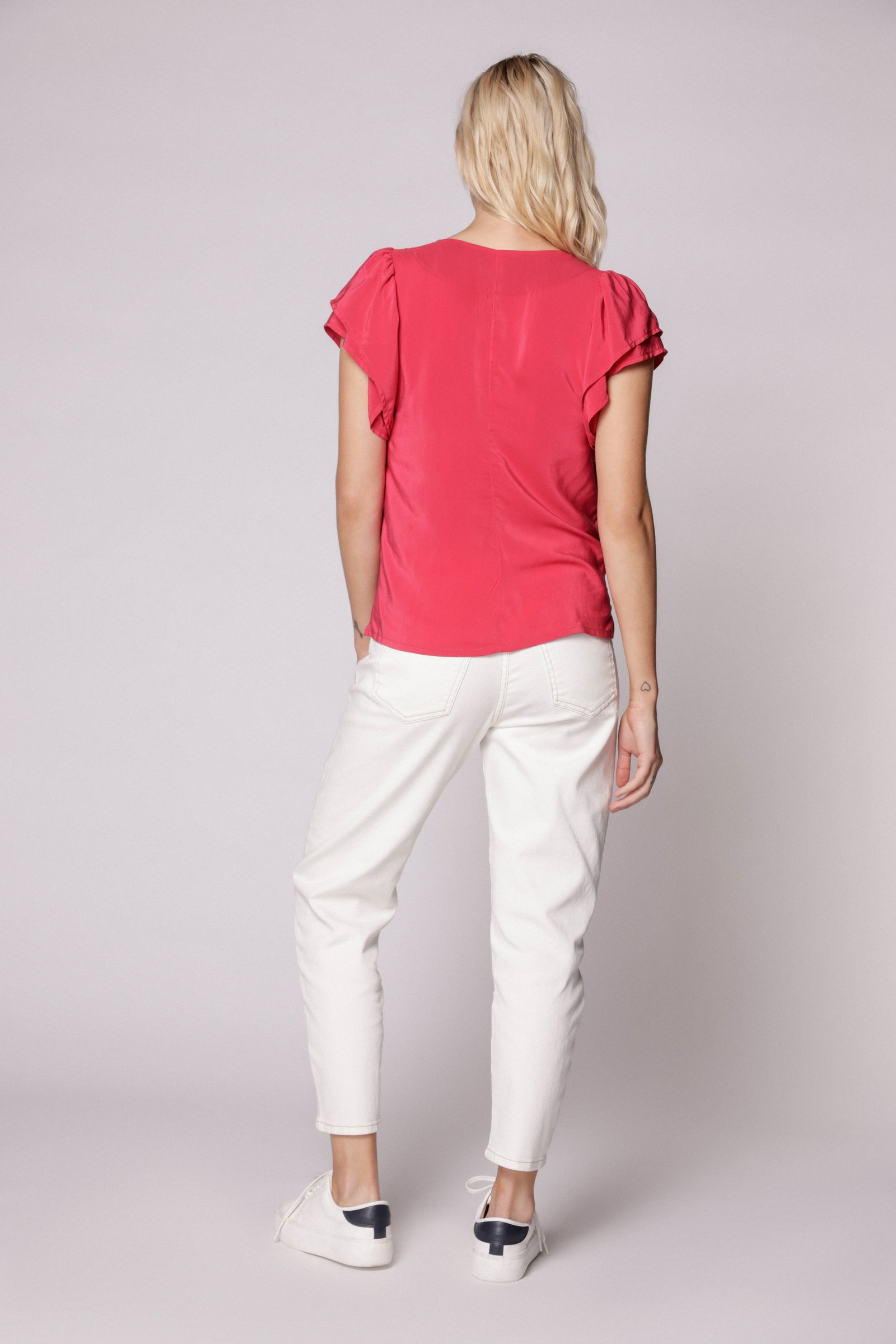 Modelo usando jeans mom fit blanco con blusa fucsia y zapatillas blancas