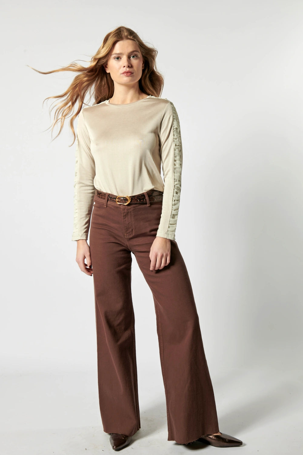 Modelo usando jeans culotte liso color café profundo con blusa beige y cinturón ancho
