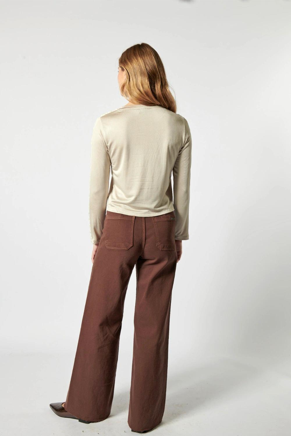 Modelo usando jeans culotte liso color café profundo con blusa beige y cinturón ancho
