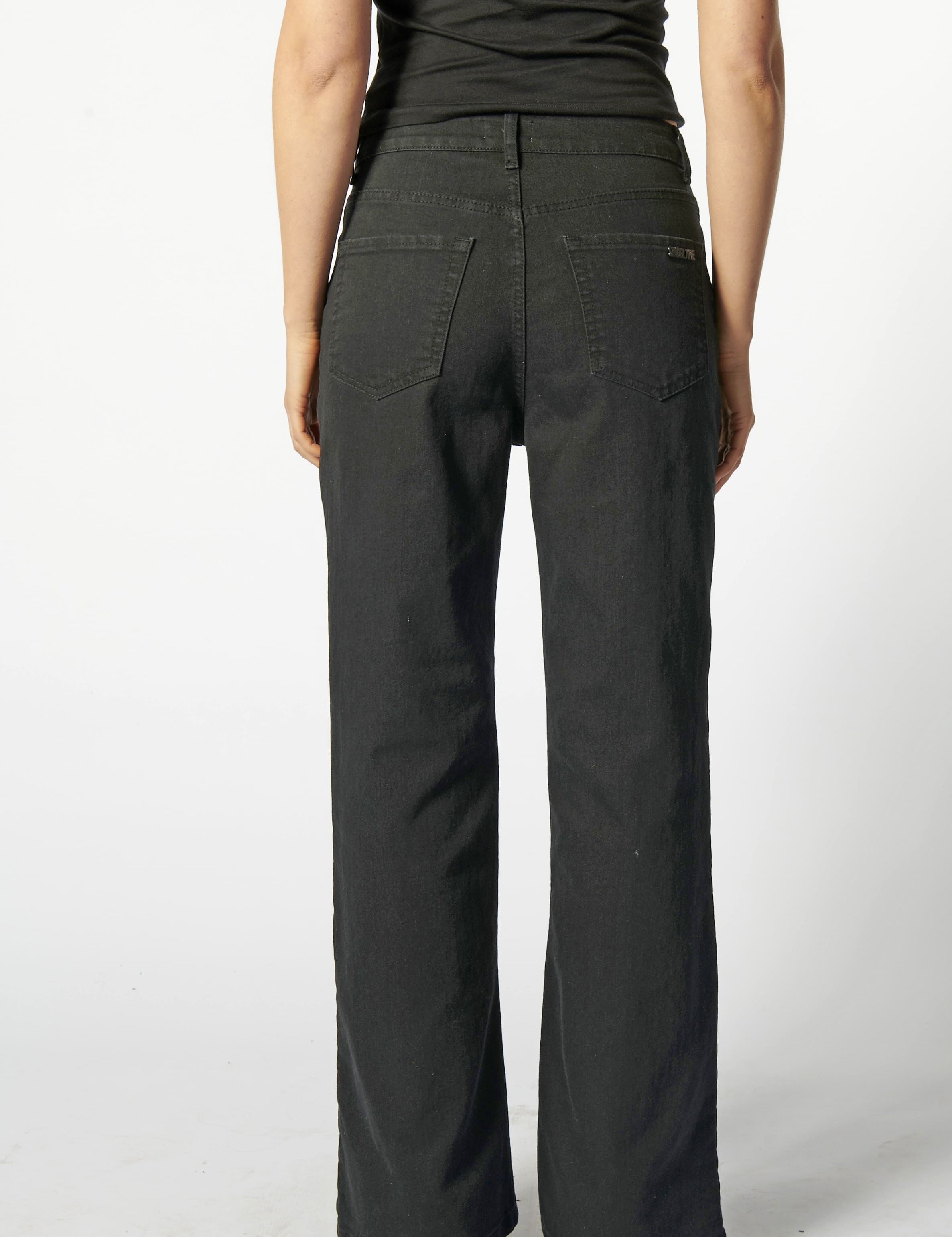 Vista trasera de jeans flare negro con logo minimalista "Singolare" en el bolsillos de parche derecho y costuras en contraste