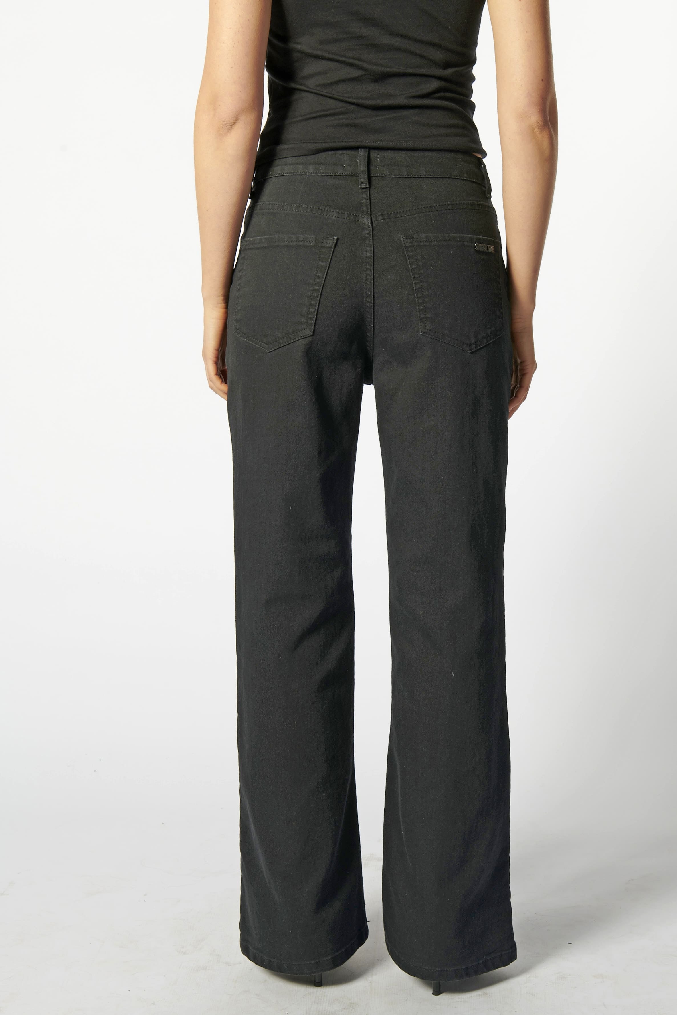 Vista trasera de jeans flare negro con logo minimalista "Singolare" en el bolsillos de parche derecho y costuras en contraste
