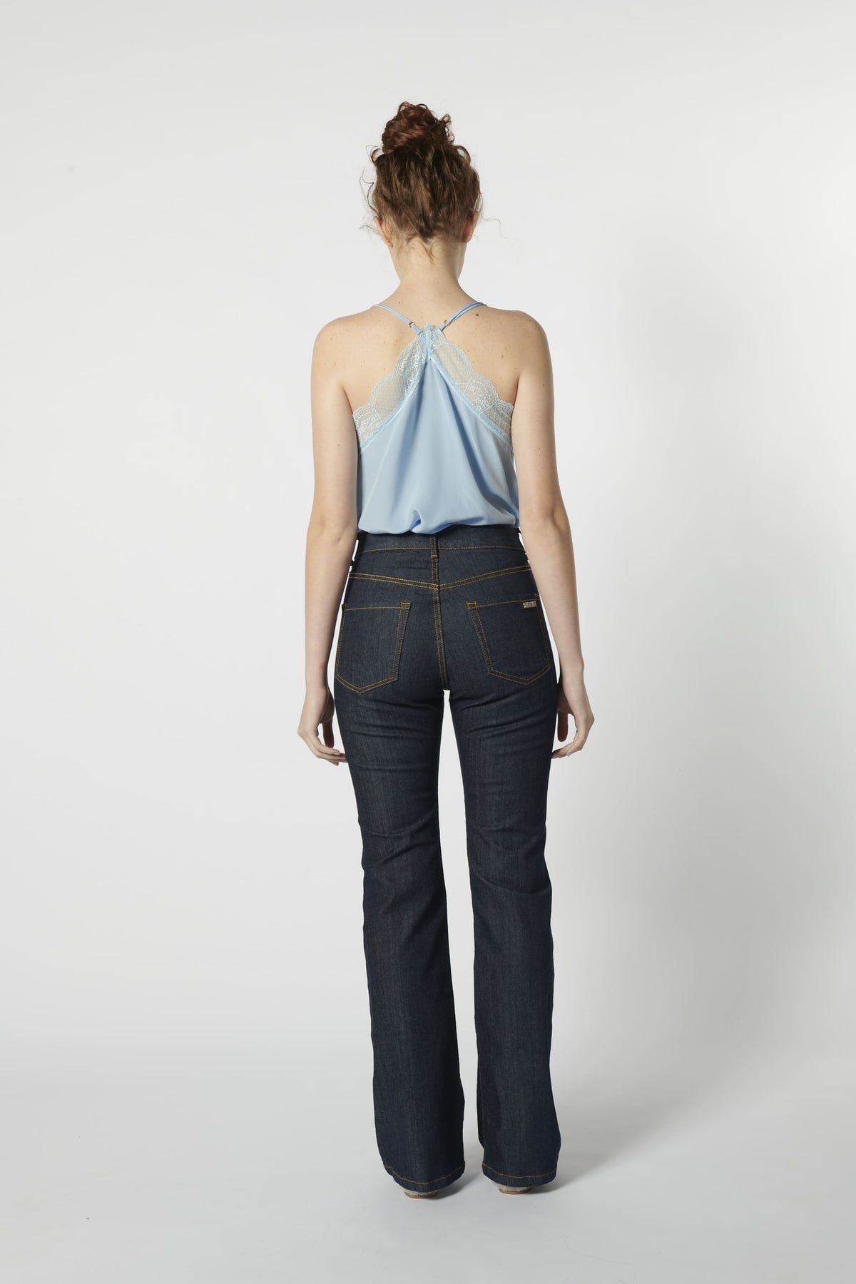 Vista trasera de jeans flare azul oscuro con top de tirantes cruzado de color celeste