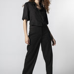 Modelo usando pantalón Parla negro con camisa negra, pretina cruzada y calce recto
