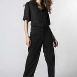 Modelo usando pantalón Parla negro con camisa negra, pretina cruzada y calce recto
