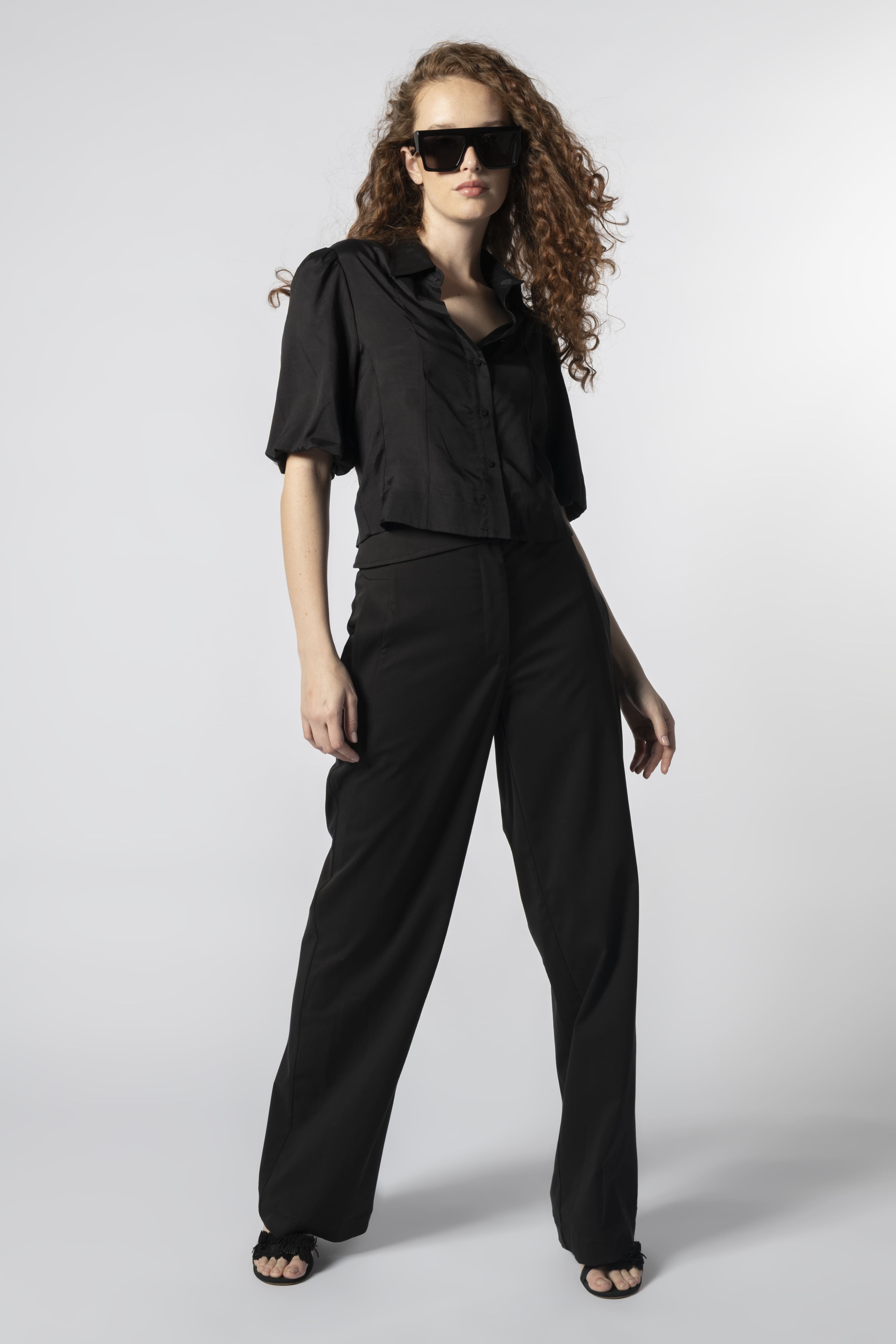 Modelo usando pantalón Parla negro con camisa negra, pretina cruzada y calce recto
