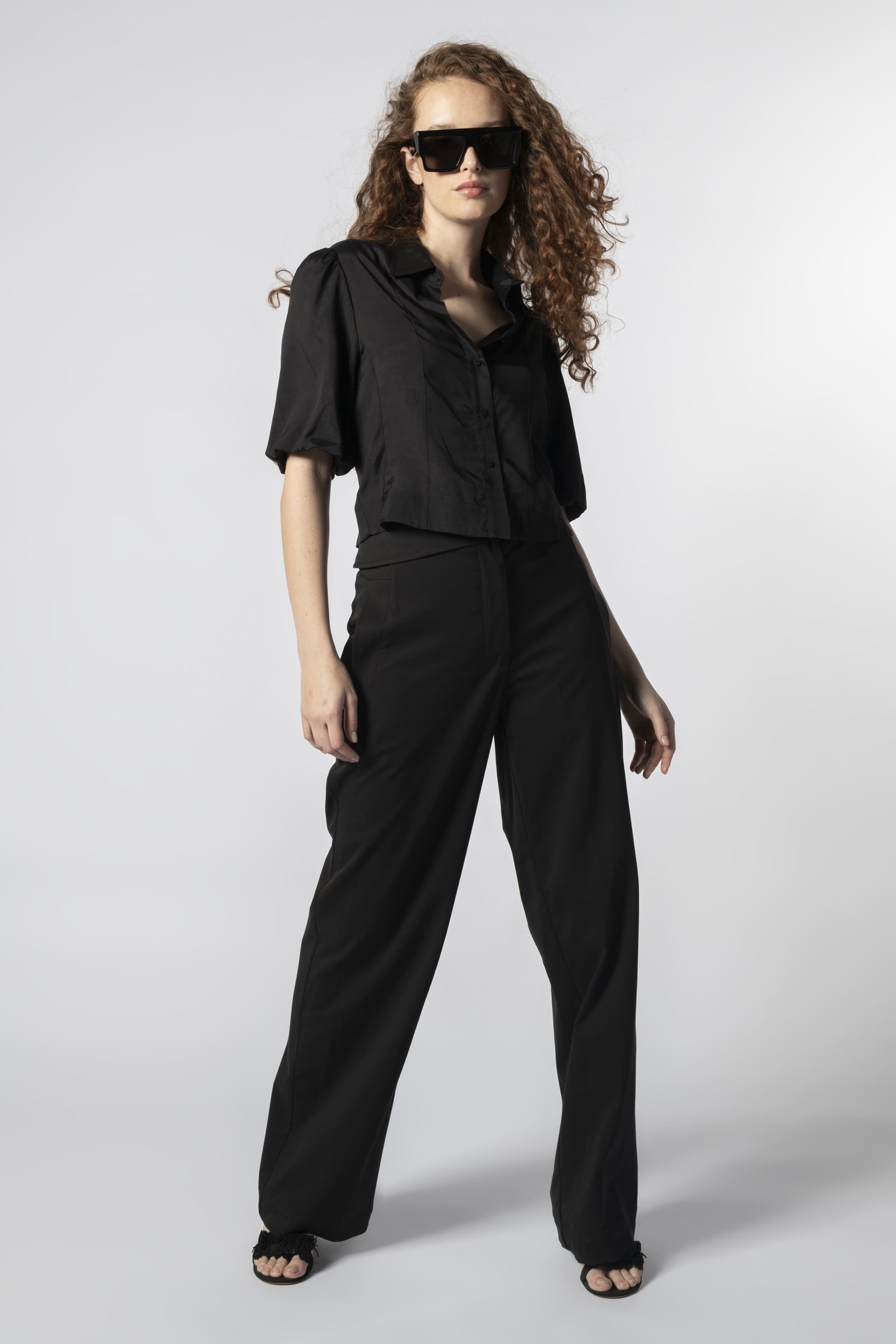 Modelo usando pantalón Parla negro con camisa negra, pretina cruzada y calce recto
