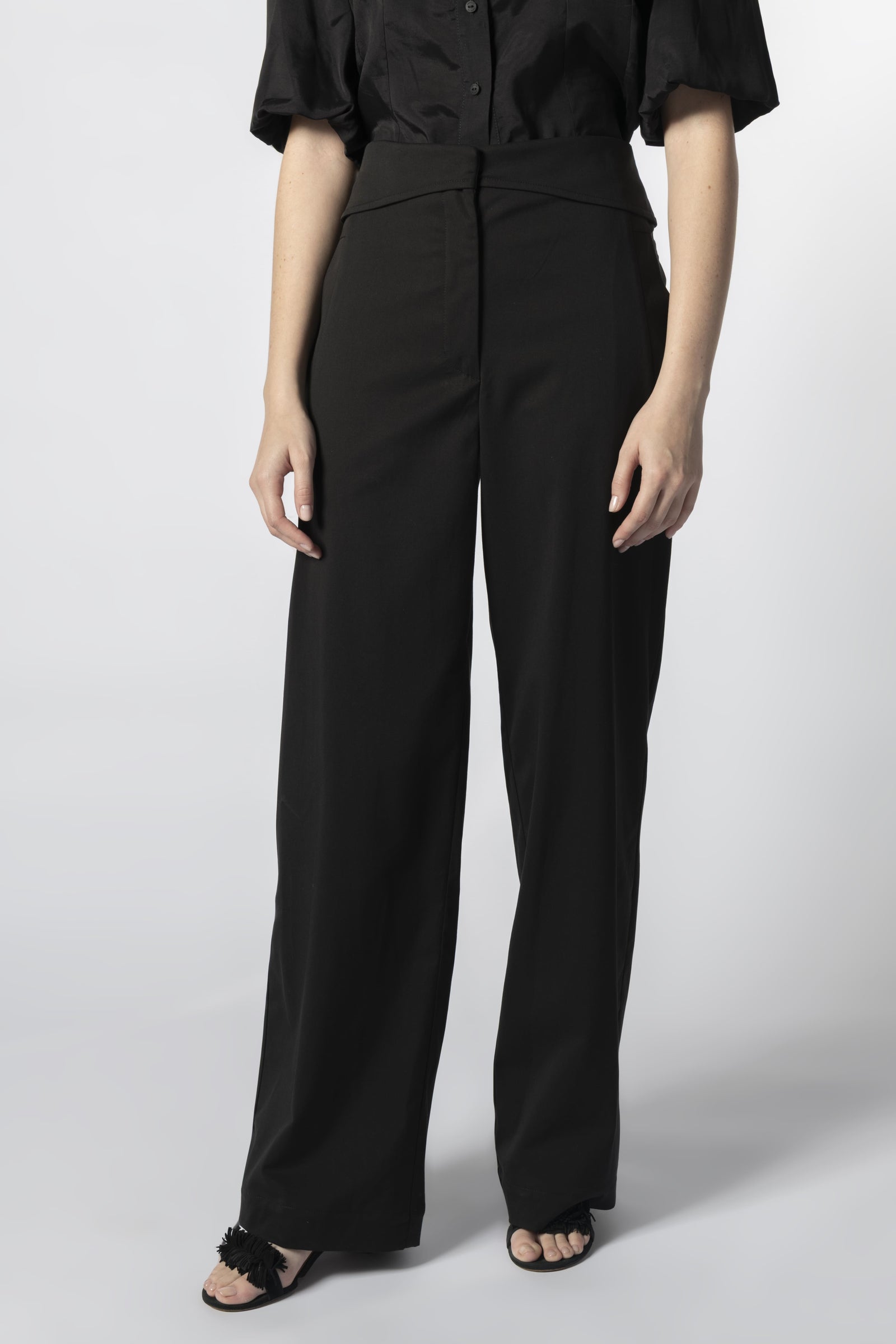 Modelo usando pantalón Parla negro con camisa negra, pretina cruzada y calce recto
