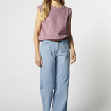 Modelo con jeans relajado color celeste claro y polera sin mangas morada, pierna semi flectada