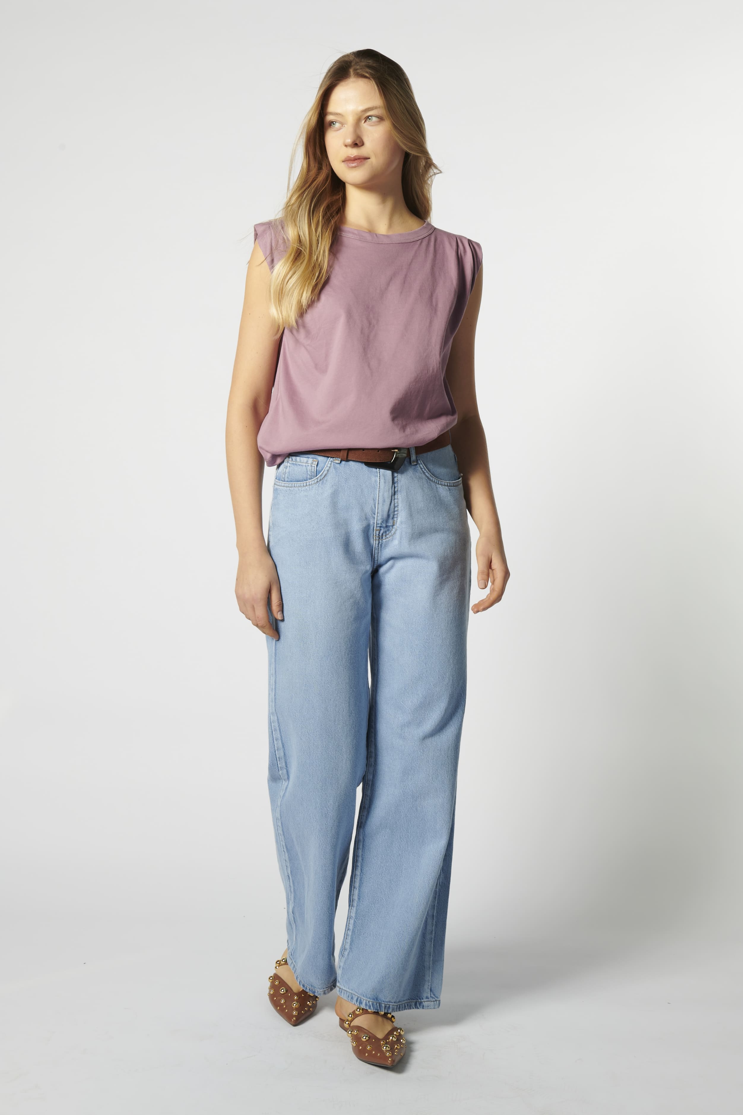 Modelo con jeans relajado color celeste claro y polera sin mangas morada, pierna semi flectada