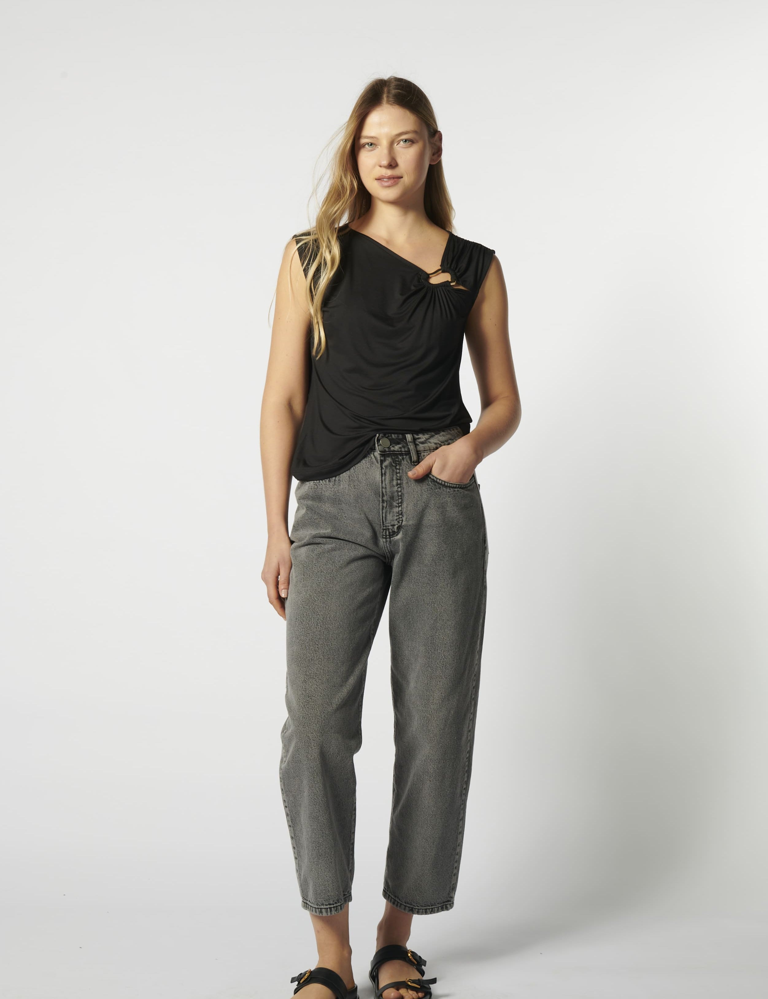 Modelo con jeans barrel gris y blusa sin mangas negra, vista frontal
