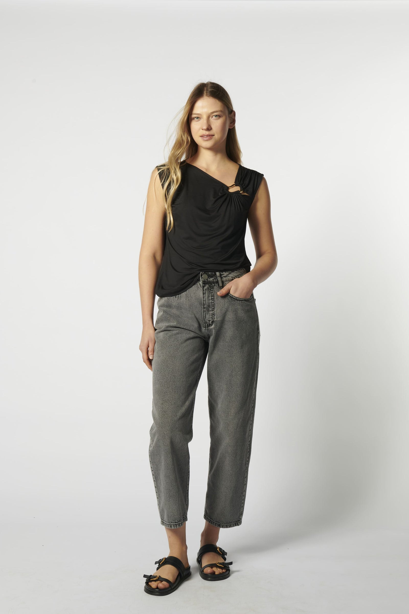 Modelo con jeans barrel gris y blusa sin mangas negra, vista frontal
