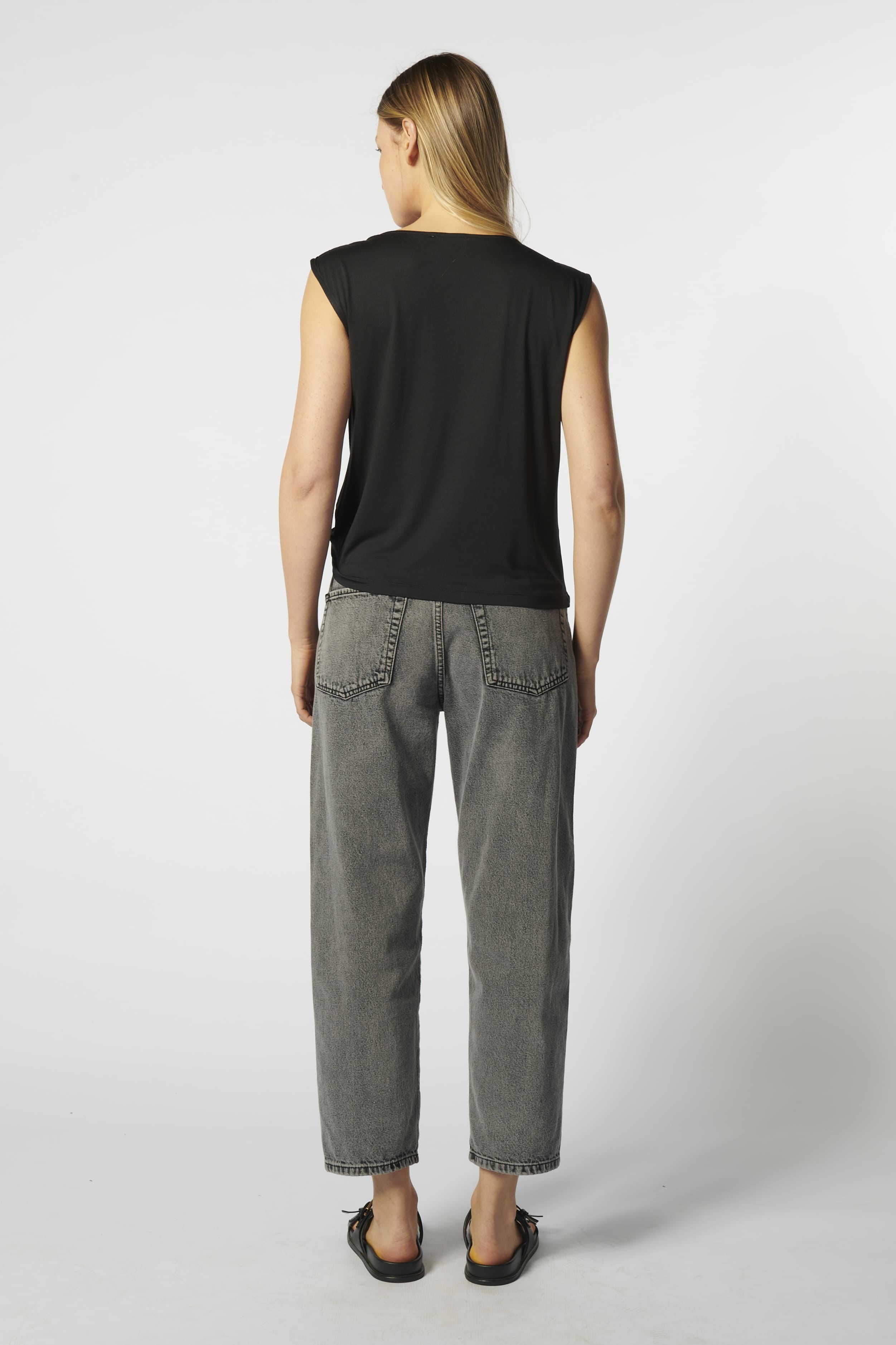 Vista trasera jeans barrel gris con blusa sin mangas negra
