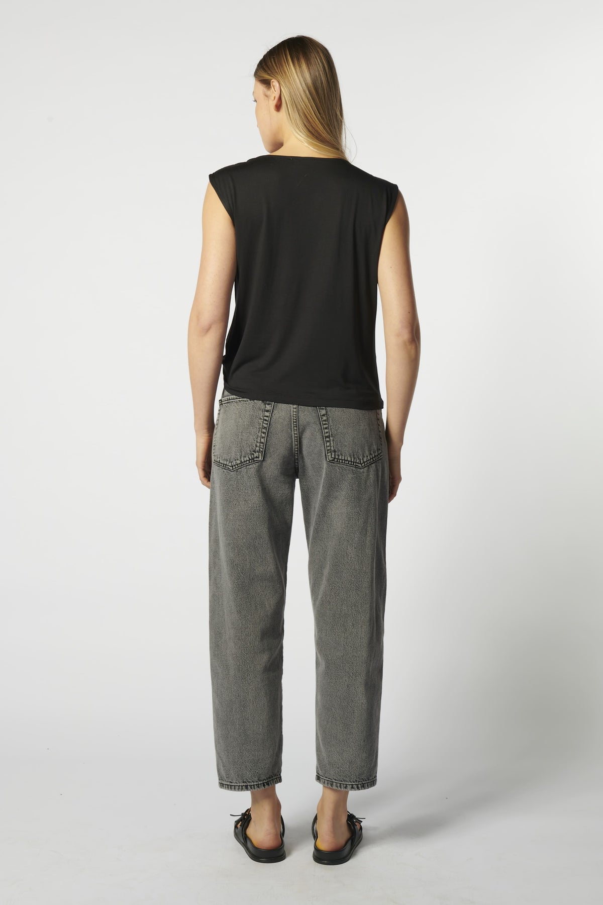 Vista trasera jeans barrel gris con blusa sin mangas negra
